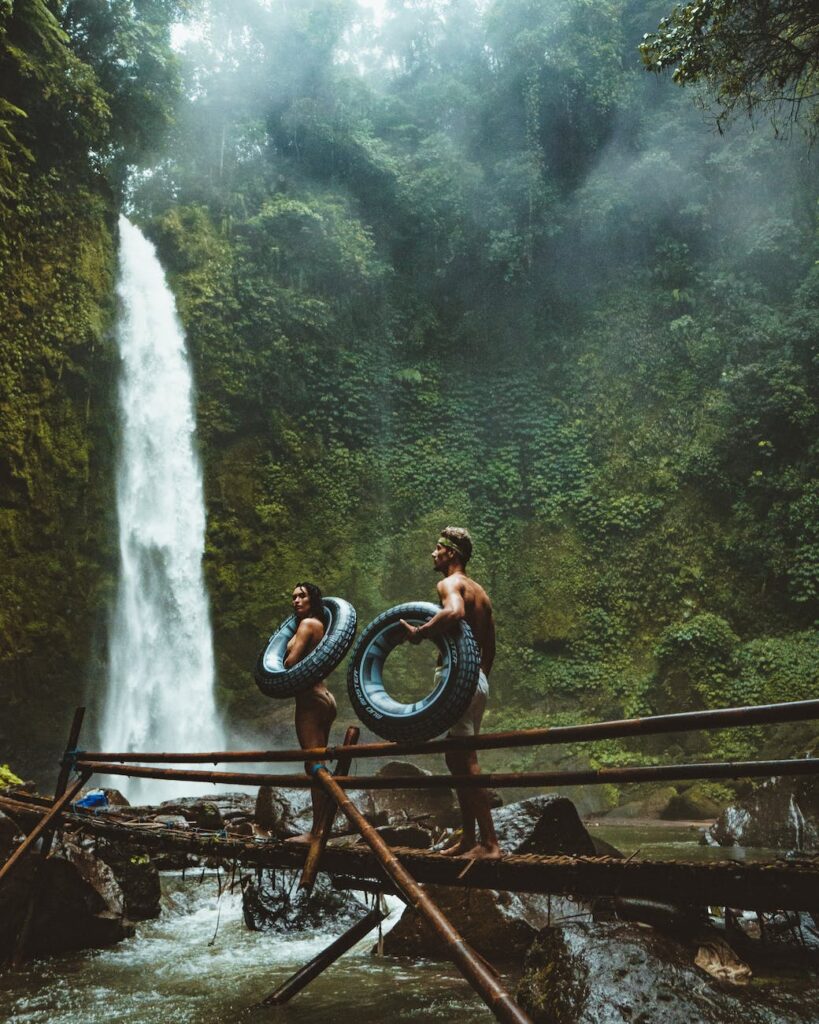 two person carrying black inflatable pool float on brown wooden bridge near waterfalls