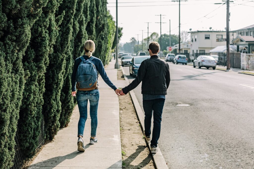 man holding woman while walking on sidewalk