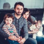 man and woman carrying babies while sitting on chair