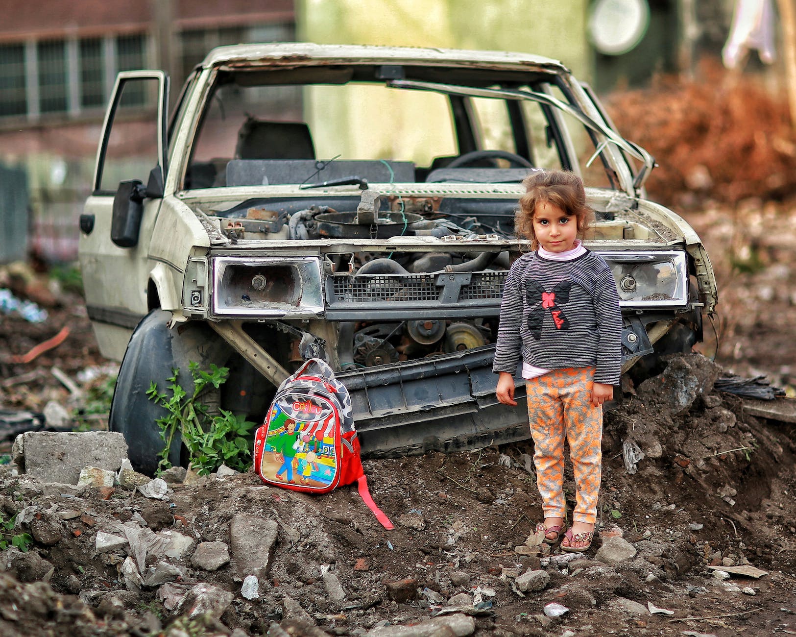 girl with backpack near broken car ruins