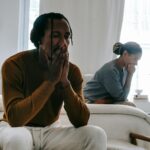 unhappy black couple sitting on bed after having argument