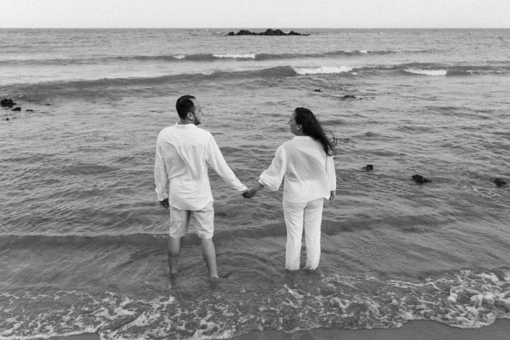 couple in white stand in sea and hold hands