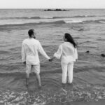 couple in white stand in sea and hold hands